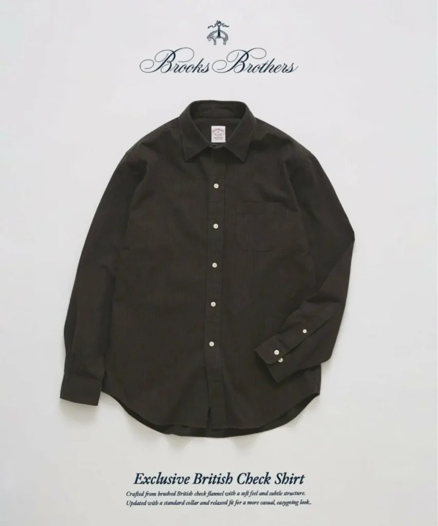 Front studio image of a Brooks Brothers Exclusive British Check Shirt in a dark charcoal brushed flannel with a subtle tonal check pattern. The shirt features a relaxed silhouette, point collar, chest pocket, white buttons, buttoned cuffs, and a rounded hem, photographed against a clean light gray backdrop