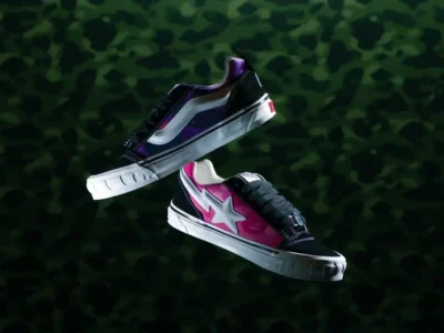 Floating pair of BAPE STA x Vans Old Skool-inspired shoe featuring pink and purple camouflage canvas, black suede overlays, white star and side stripe logos, chunky serrated white foxing, and metallic lace hardware against a dark camouflage backdrop