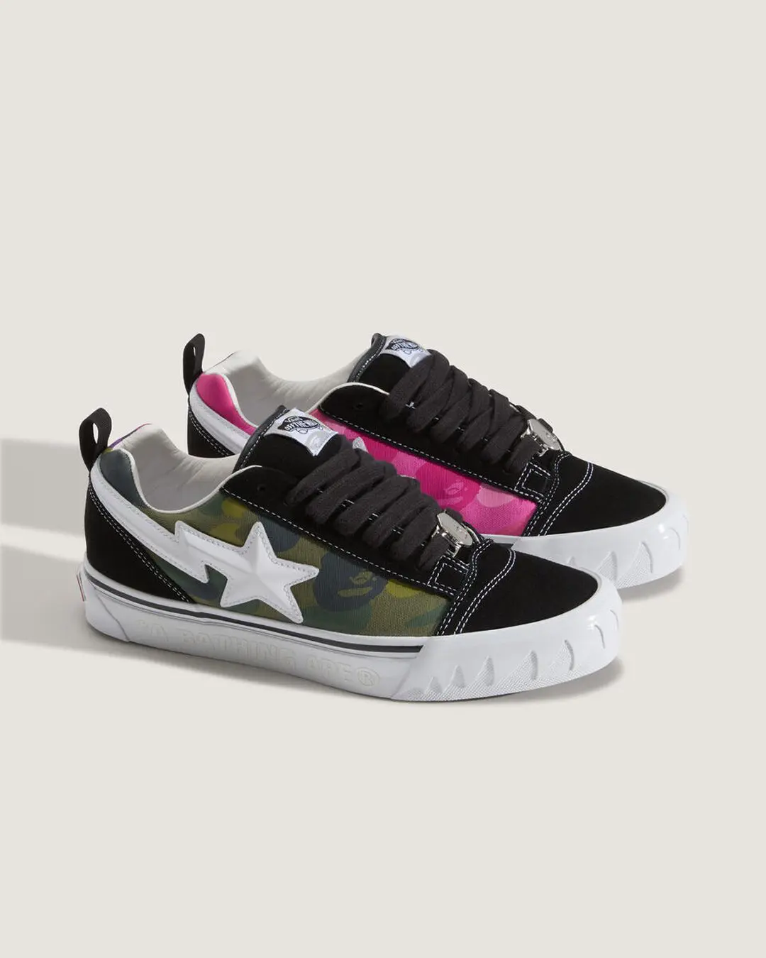 Studio image of two BAPE x Vans Old Skool sneakers featuring olive and pink ABC Camo canvas panels, black suede overlays, oversized white STA logos, chunky serrated white midsoles, thick black laces, and metallic lace hardware on a light beige background.