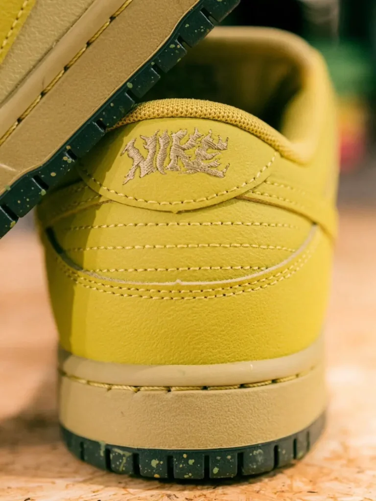 Rear heel detail of the Nike SB Dunk Low Pro showing tonal embroidered Nike branding above layered yellow leather panels and a black speckled outsole