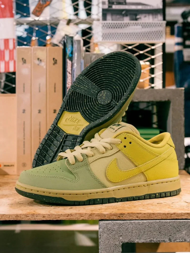 Side profile of the Nike SB Dunk Low Pro on a wooden display, with the second shoe showing the black speckled outsole and skate-inspired tread pattern in the background