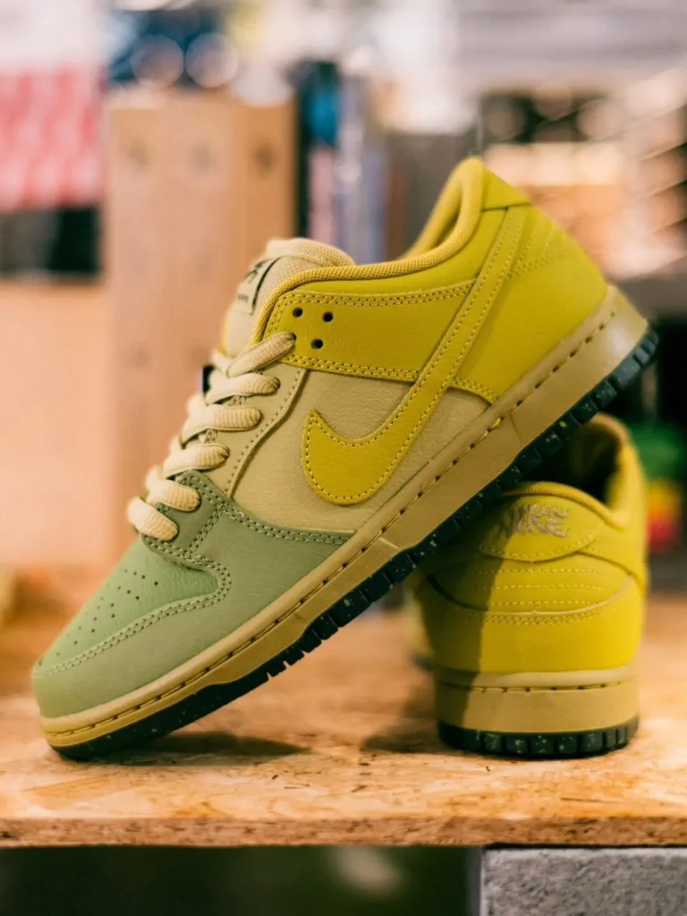 Pair of Nike SB Dunk Low Pro shoe posed heel-to-toe, showcasing the layered yellow, cream, and sage green leather panels with cream laces and a speckled black outsole