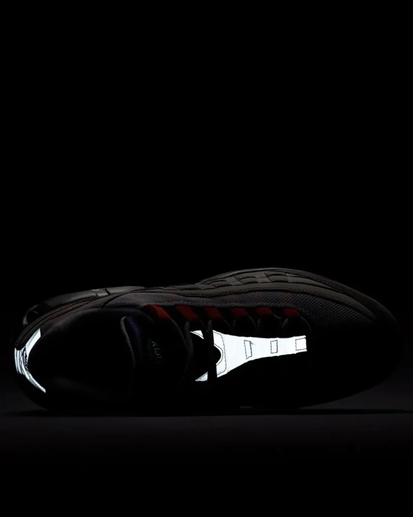 Reflective side profile of a Nike Air Max 95 in low light, highlighting the bright reflective tongue strip, heel tab, and upper details with view Air Max cushion