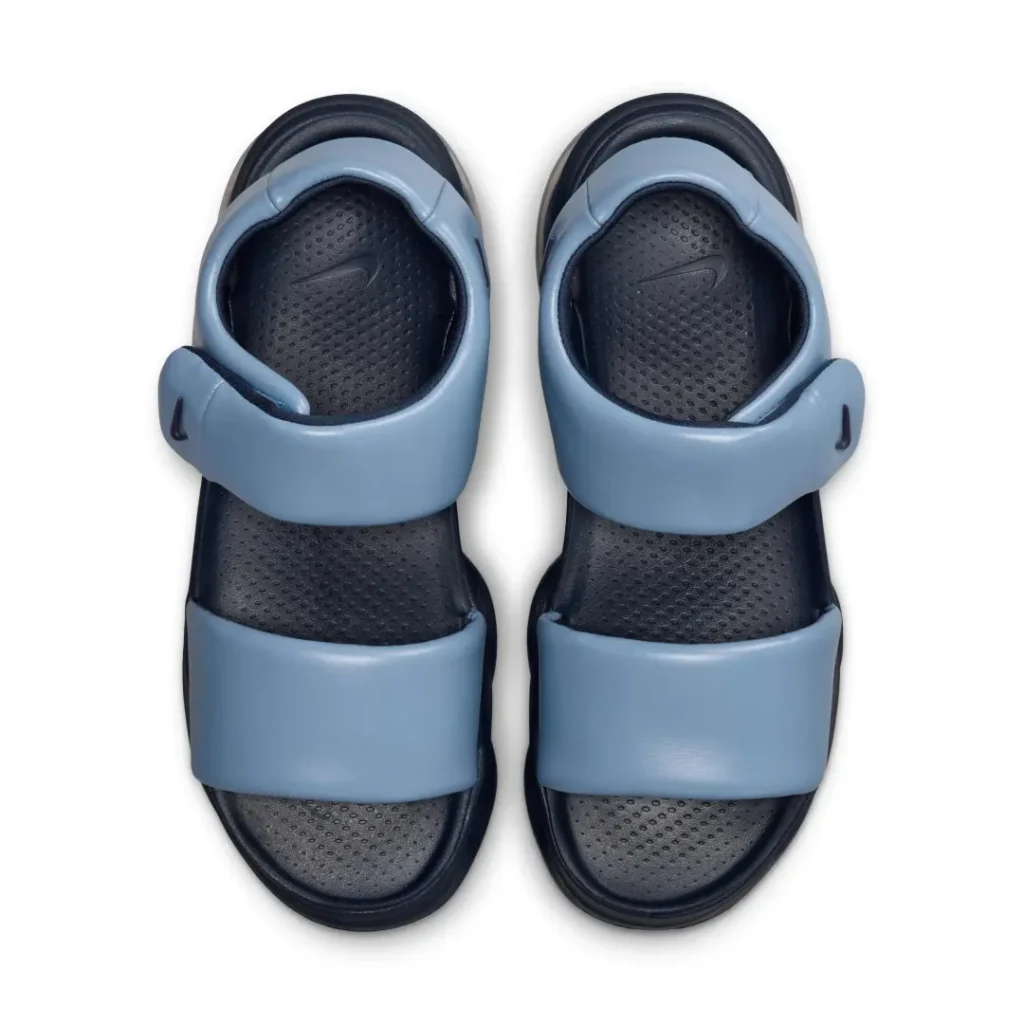 Top-down view of the Nike Air Max platform sandals placed side by side. The image highlights the perforated dark navy footbeds with molded Nike Swoosh logos, padded light blue forefoot straps, adjustable ankle closures, and the ergonomic foot shape designed for comfort and support