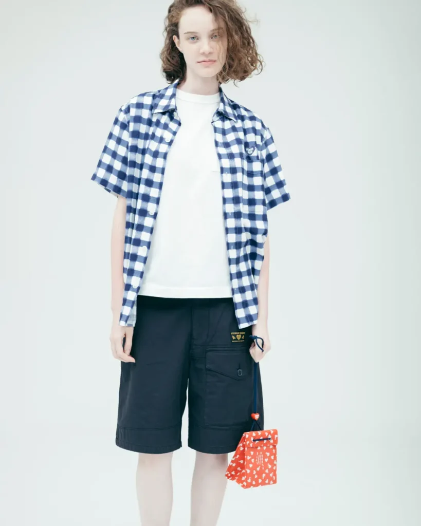 udio portrait of a model wearing a blue gingham Human Made short-sleeve shirt, white tee, black shorts, and a red patterned drawstring pouch