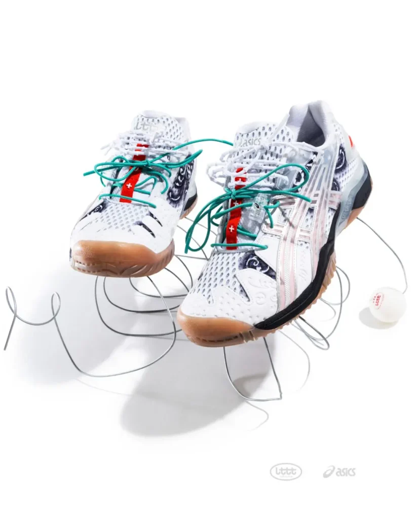 Front three-quarter view of the white ASICS x Lttt table tennis shoes on a white background, emphasizing the gum outsole, perforated mesh upper, translucent side cage, and green lace overlay