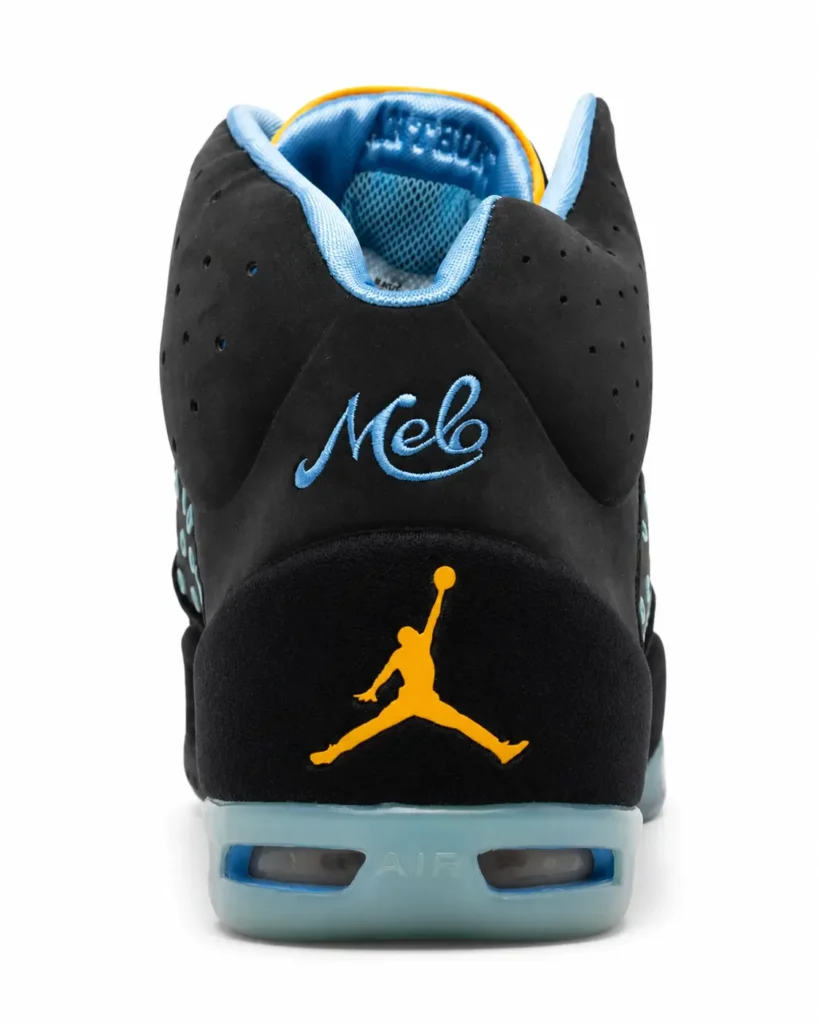 Rear view of a black Jordan Melo basketball shoe against a white background. The heel features embroidered powder blue "Melo" script above a gold Jumpman logo, with a translucent icy blue Air cushioning unit and light blue padded collar accented by a thin yellow trim