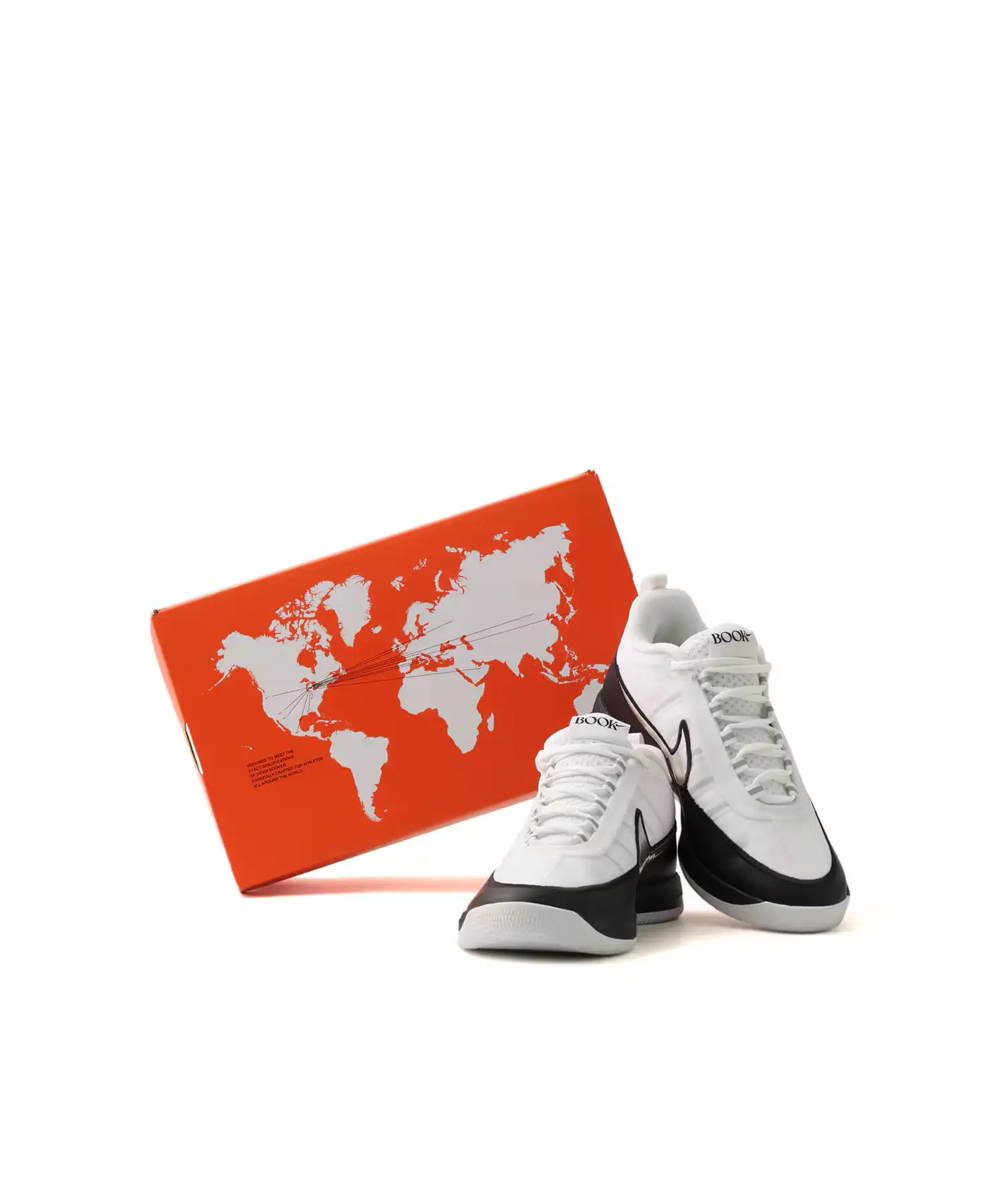 Nike BOOK Chapter Two sneakers in a white and black colorway displayed beside the bright orange collector's shoebox featuring a world map graphic, highlighting the travel-inspired packaging and clean low-top design.