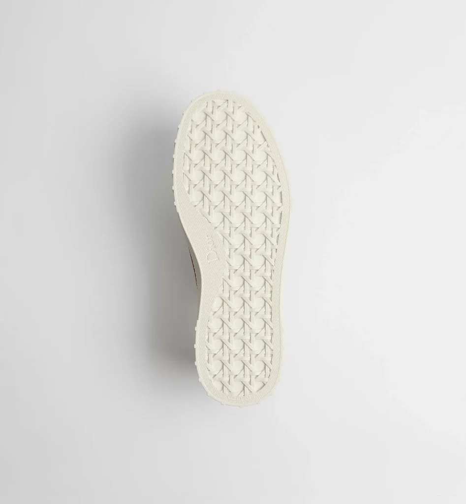 Bottom view of the sneaker displaying an off-white rubber outsole with an all-over geometric woven tread pattern, embossed Dior branding at the midfoot, and a clean monochrome finish