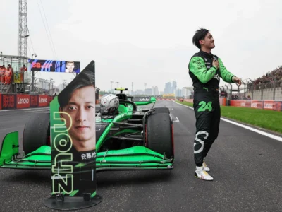Zhou Guanyu stands beside his green Formula 1 car on the starting grid, acknowledging the crowd with his hand over his chest as fans fill the grandstand