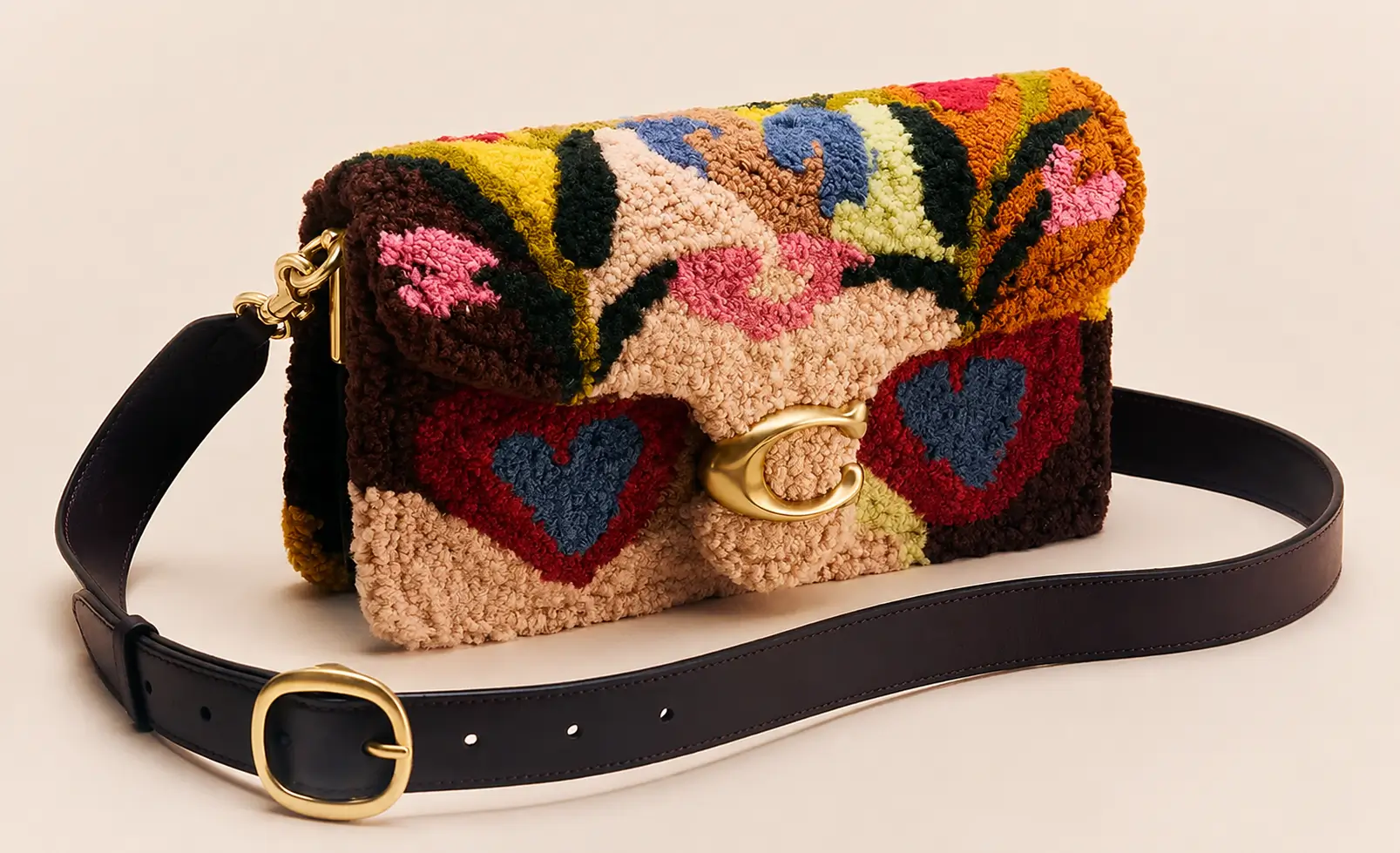 Coach Tabby shoulder bag in multicolored artisan tufted textile with floral and heart motifs, gold C clasp, and dark leather strap displayed on a neutral studio background.
