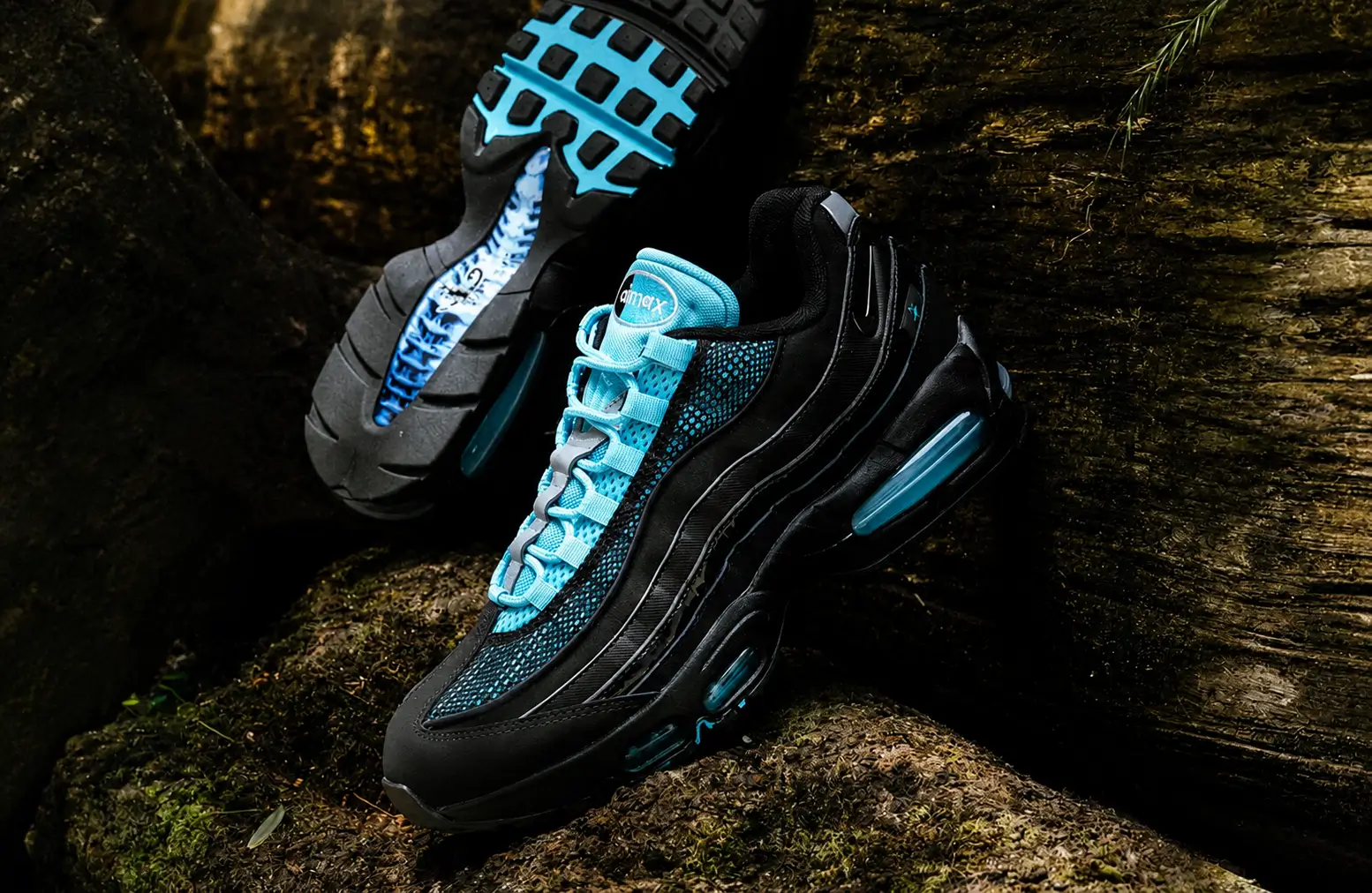 Nike Air Max 95 in a black and aqua colorway displayed on moss-covered rocks in a forest setting, featuring bright aqua mesh panels, glossy black overlays, visible blue-tinted Air Max cushioning, and a rugged outdoor backdrop that highlights the shoe's scorpion-inspired design.