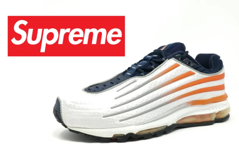 White and navy Supreme x Nike running shoe with bold orange side stripes, sculpted ribbed overlays, black outsole, and a sleek aerodynamic silhouette against a clean white background, with a partial Supreme box logo view on the left