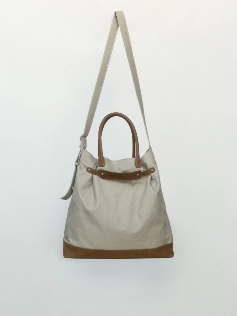 Large canvas tote bag with leather trim and top handles, featuring an adjustable shoulder strap and a neutral beige colorway