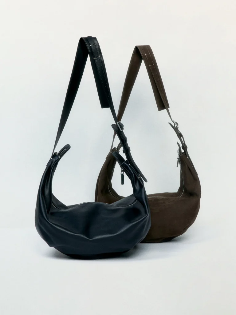 Two crescent-shaped shoulder bags in black leather and dark brown suede with adjustable straps and minimal zip-top construction
