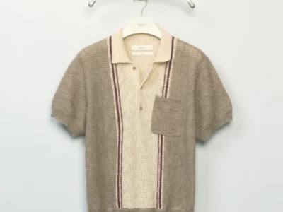 Short-sleeve knit polo in beige and cream with vertical striped detailing, ribbed texture, and a patch chest pocket on a hanger