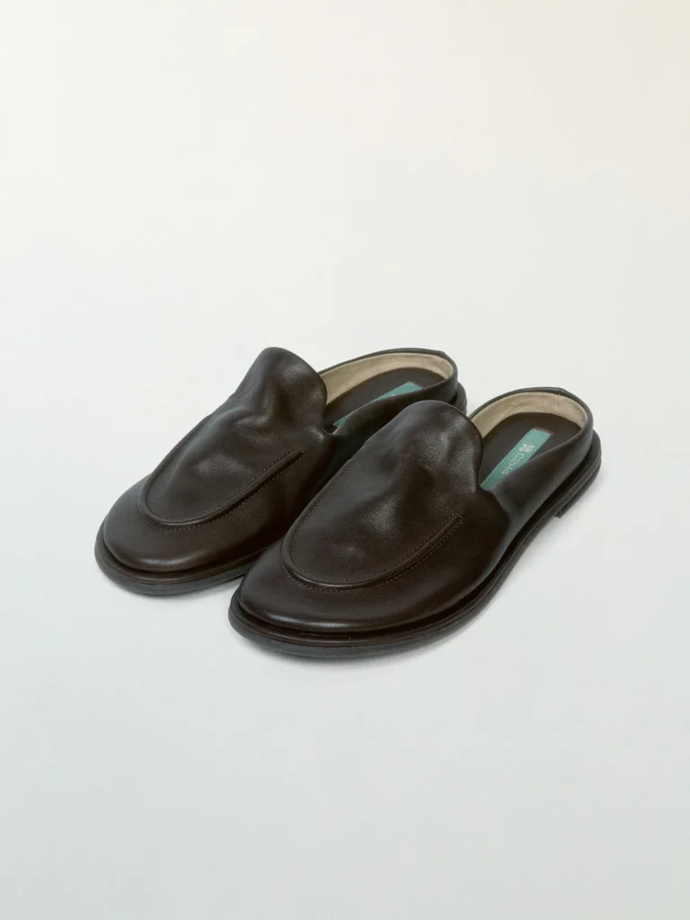 Pair of black leather backless loafers with a smooth matte finish, rounded moc-toe construction, and low-profile sole