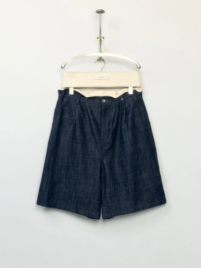 Dark indigo pleated shorts with a tailored wide-leg fit, belt loops, and front button closure displayed on a hanger