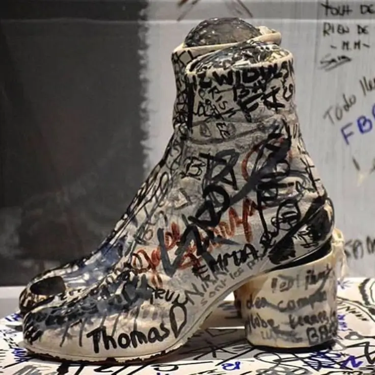 Hand-painted Maison Martin Margiela Tabi ankle boot prototype covered in handwritten notes, sketches, signatures, and experimental markings, displayed as part of the designer's personal archive.