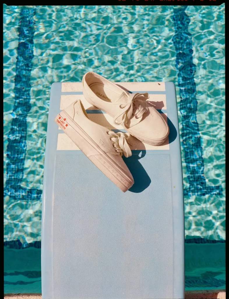 Pair of cream canvas shoe displayed on a blue pool slide above sparkling turquoise swimming pool water in bright sunlight
