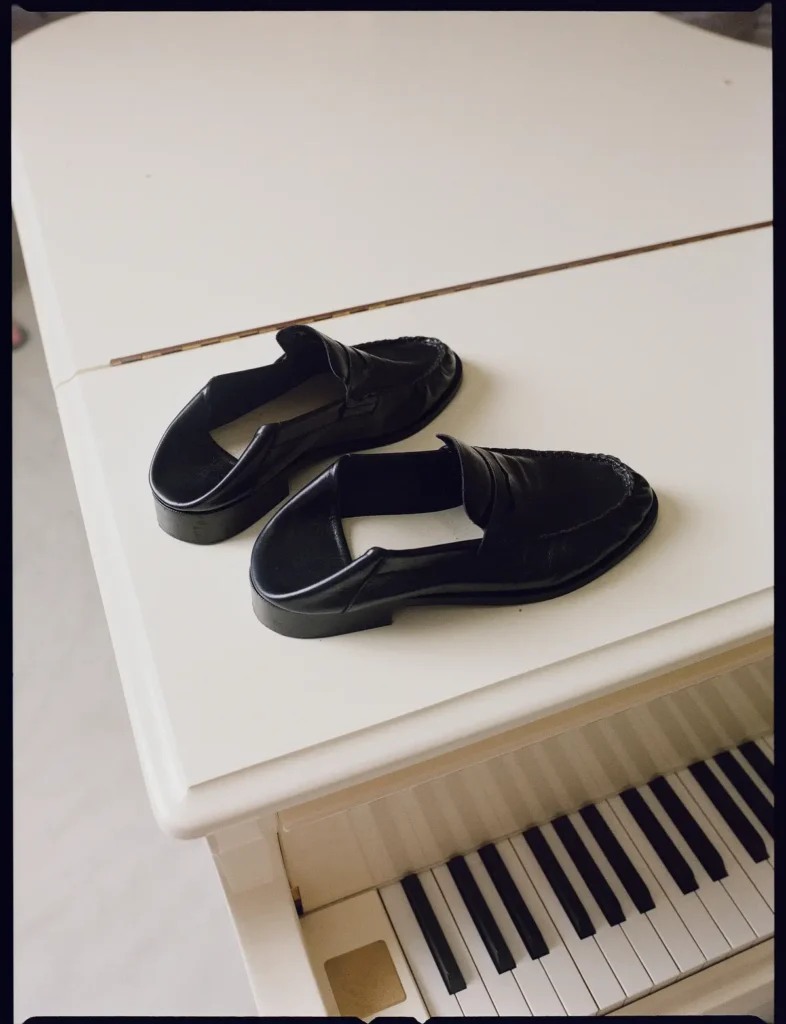 Pair of polished black leather penny loafers displayed on top of a white grand piano with piano keys view below