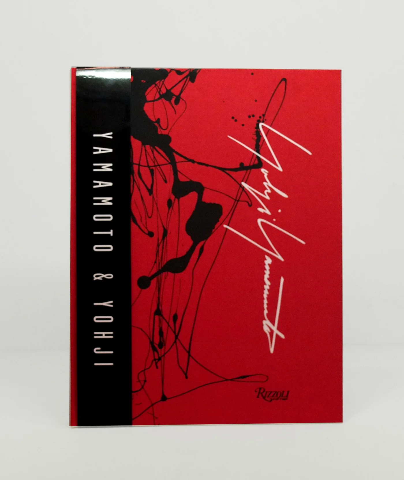 Cover of the Yohji Yamamoto & Yohji book featuring a vivid red background with abstract black ink splatters, the designer's white signature, and a black vertical title band.
