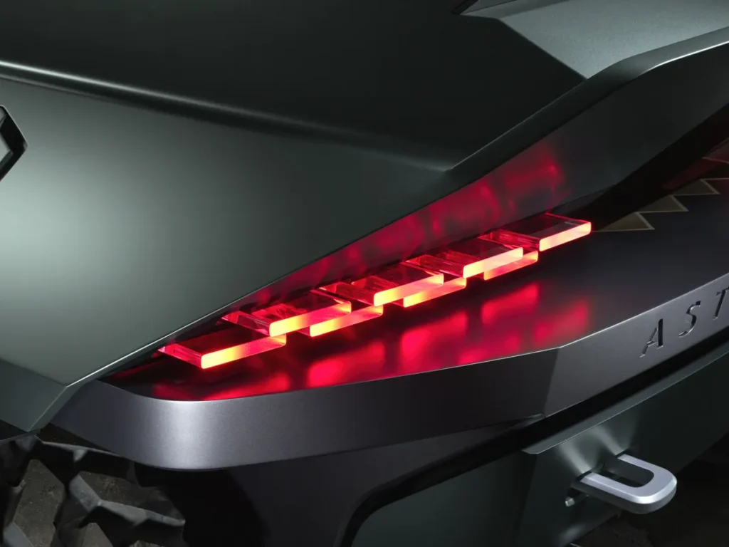 Close-up of the truck's rear lighting, featuring a slim horizontal taillight with illuminated segmented LED elements tucked beneath an angular overhanging body panel, finished with a dark metallic bumper and integrated recovery point