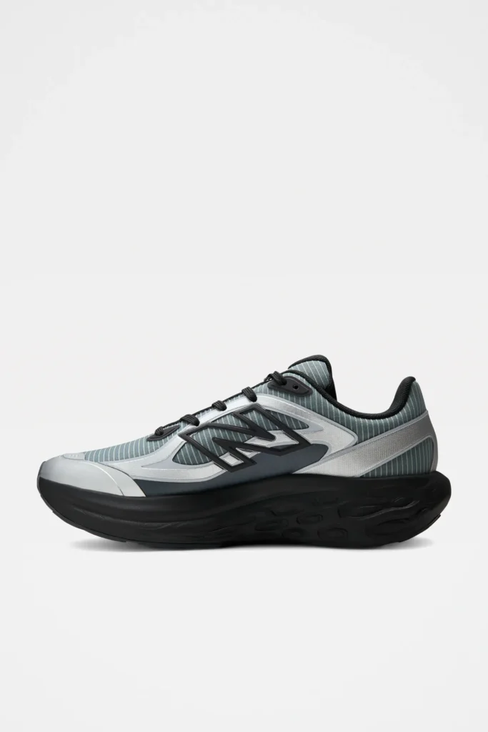 Opposite side profile of the New Balance performance running shoe showcasing the streamlined striped mesh upper, silver synthetic overlays, sculpted black Fresh Foam X midsole, and minimalist white backdrop
