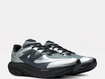 Three-quarter front angle of a pair of New Balance running shoes highlighting the striped gray-green mesh uppers, metallic silver toe caps, oversized black "N" logos, black laces, and thick Fresh Foam X cushion