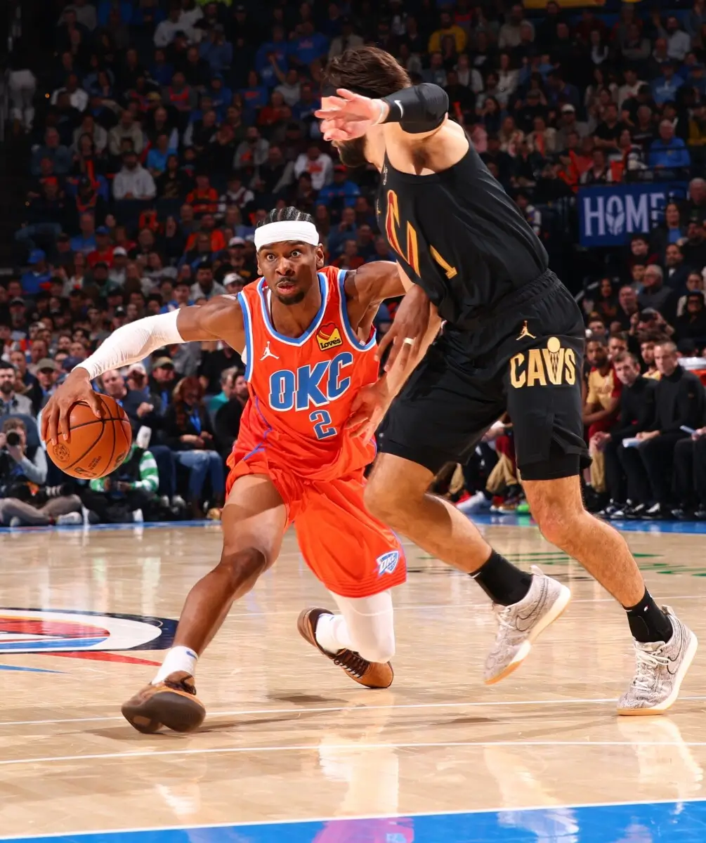 Oklahoma City Thunder guard Shai Gilgeous-Alexander drives past a Cleveland Cavaliers defender during an NBA game, wearing the Converse SHAI 001 PREMIUM: Slither in a snakeskin-inspired finish. The action shot captures his low dribble, explosive first step, and the signature footwear in live game play.