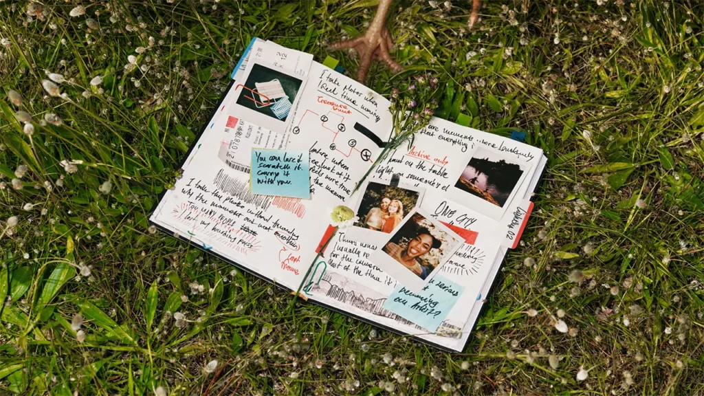Open travel journal filled with handwritten notes, instant photographs, tickets, and colorful sticky notes lying on green grass, capturing memories created with the Polaroid Flip