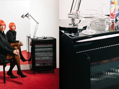 Split composition showing two people in matching black outfits and bright orange bob wigs seated beside the black cabinet on a red carpet, paired with a close-up of the cabinet's glassware and ribbed front panel