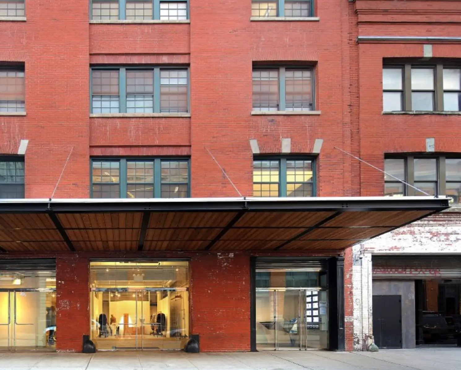 Exterior of the SKYLRK pop-up venue at 60 10th Avenue in Manhattan, featuring a red brick industrial building with a wide metal canopy and floor-to-ceiling glass storefront.