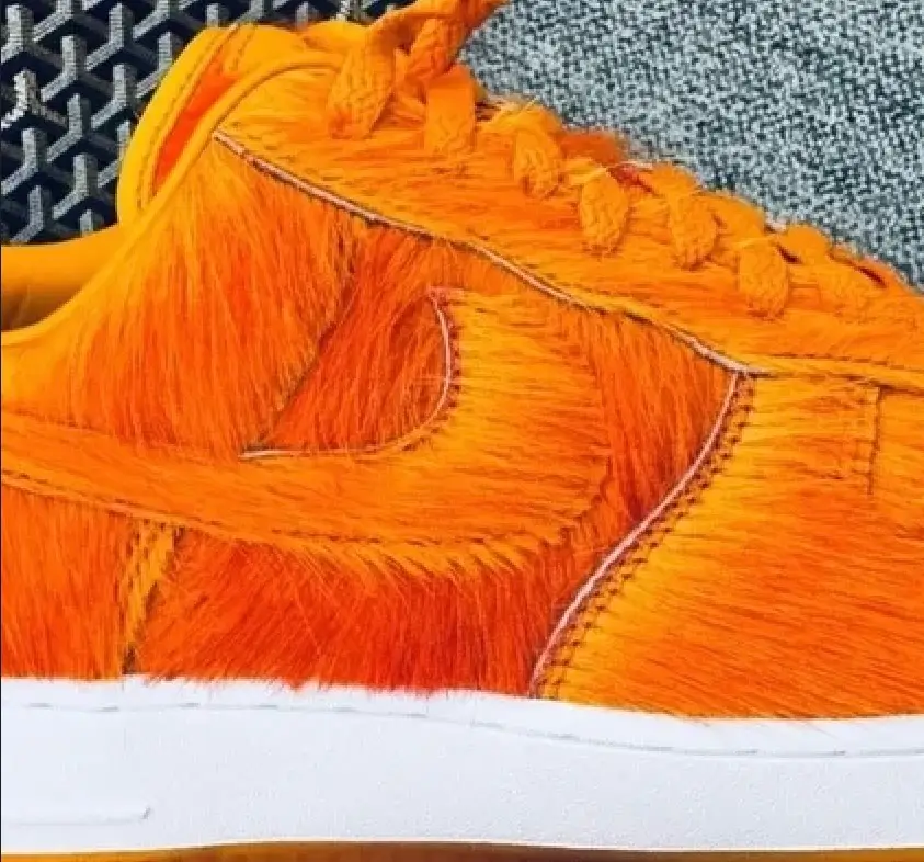Close-up of the Nike Air Force 1 sample featuring a vivid orange faux fur upper with layered shaggy panels, tonal Swoosh, white midsole, and translucent orange outsole.