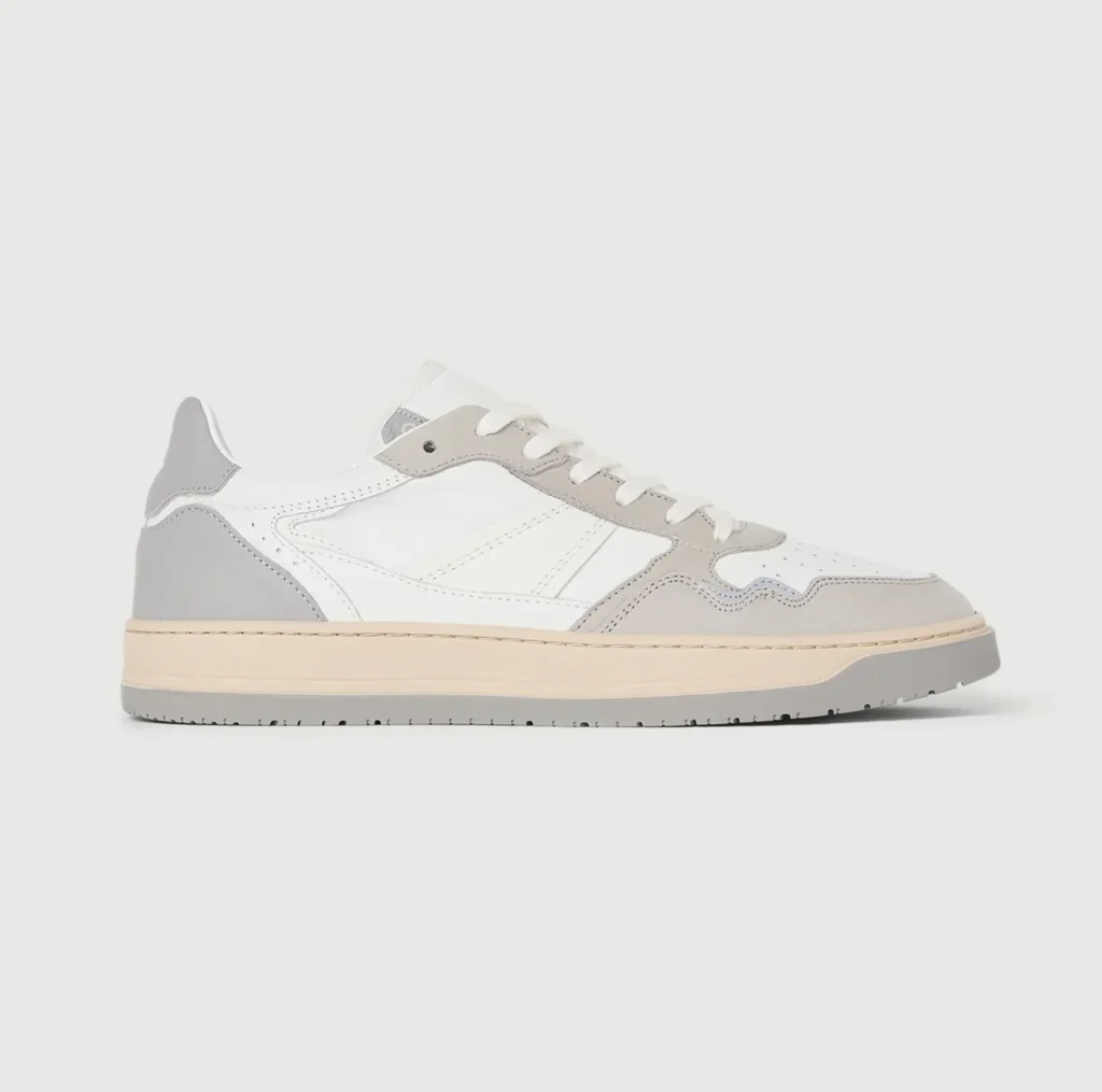 White and light gray leather low top shoe shown in lateral side profile with suede overlays, cream midsole, gray outsole, and white laces against a light gray background