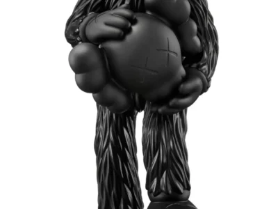 Black KAWS collectible figure standing headless while cradling its detached Companion head, with the severed neck revealing a bright red tree-ring cross section and a detached hand resting beneath one foot against a white background