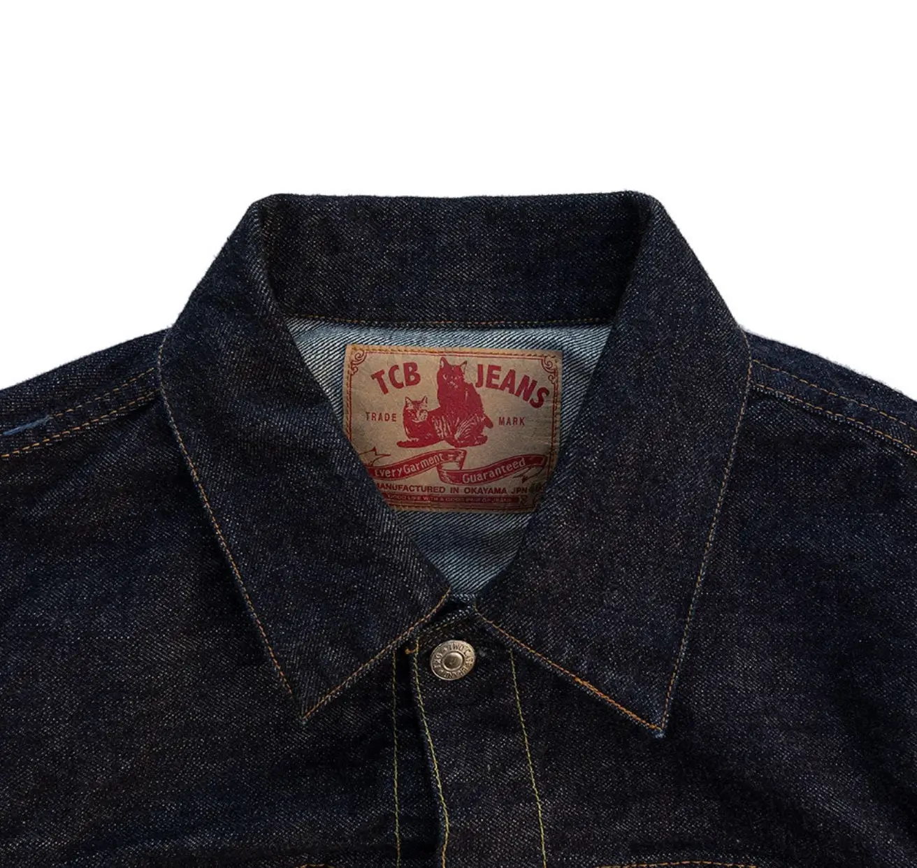 Close-up of a dark indigo selvedge denim jacket featuring a pointed collar, contrast stitching, metal top button, and a TCB Jeans leather neck label.