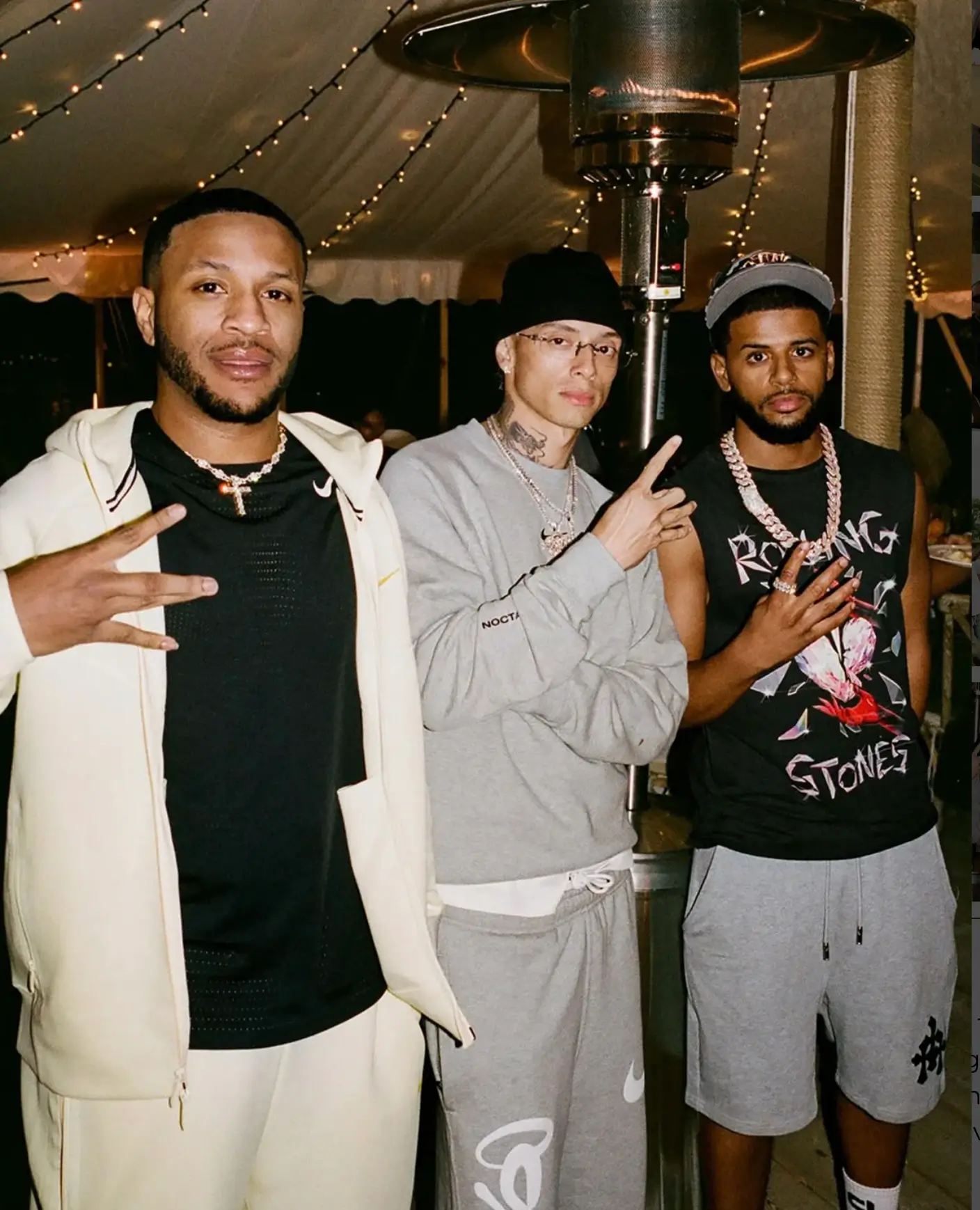 Three guests pose together inside a softly lit outdoor event tent, wearing Nike and NOCTA apparel beneath string lights and patio heaters during a nighttime gathering at NOCTA Manor.
