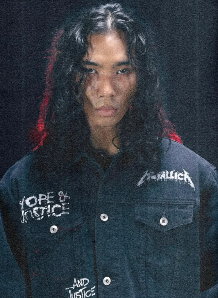 Front portrait of a model wearing a dark denim jacket customized with hand painted style Metallica graphics and "Hope & Justice" lettering across the chest. The grainy close up highlights the distressed artwork, silver buttons, and the model's long wavy hair against a black backdrop