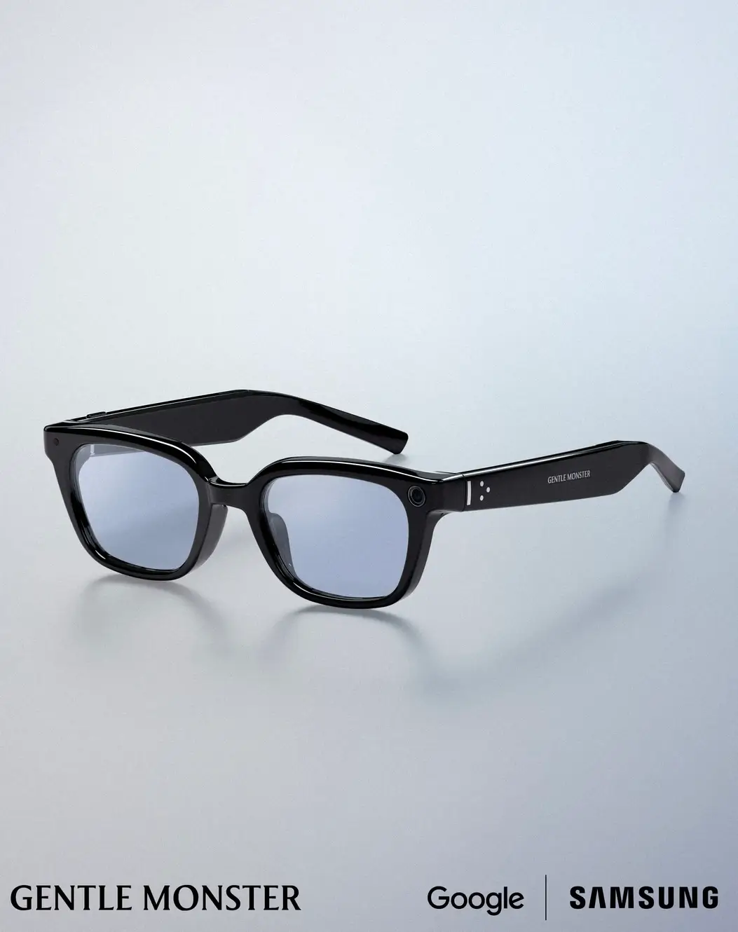 Rectangular black Gentle Monster AI smart glasses with lightly tinted lenses, glossy acetate frames, integrated camera and sensors, and subtle Samsung and Google technology, photographed on a clean white studio background.