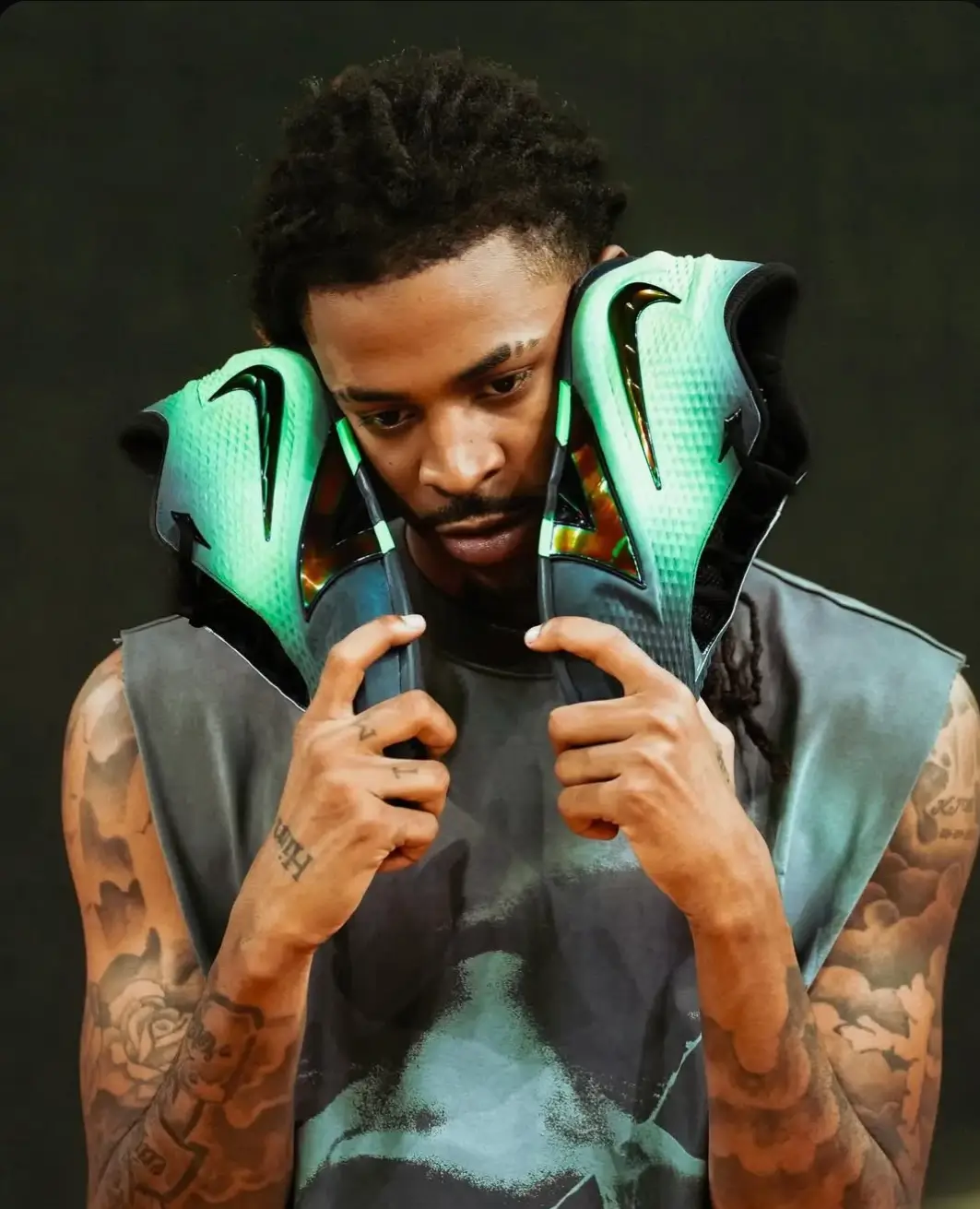 Basketball player holding mint-green and black Nike basketball shoes beside his face.