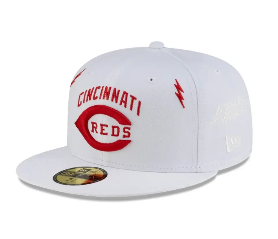 Front three-quarter view of a white Cincinnati Reds fitted cap featuring red embroidered team wordmark and classic wishbone C logo on the front, red lightning bolt embroidery on the side, tonal white New Era branding, a flat brim with a gold sizing sticker, and a clean white background.