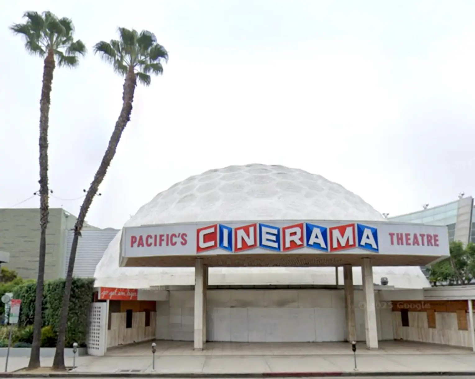 A wide-angle black-and-white photograph of an empty movie theater with rows of seats facing a glowing curved projection screen beneath a honeycomb-patterned domed ceiling.
