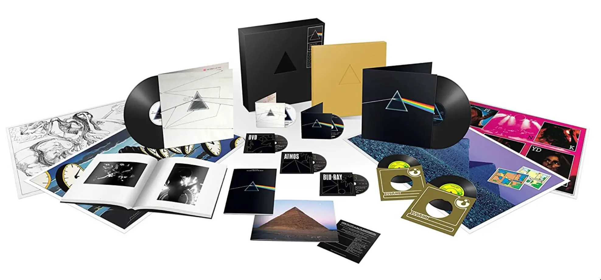 Pink Floyd The Dark Side of the Moon deluxe collector's box set displayed with vinyl records, Blu-ray and DVD discs, hardcover books, posters, art prints, photo book, postcards, and archival memorabilia arranged across a clean white background.