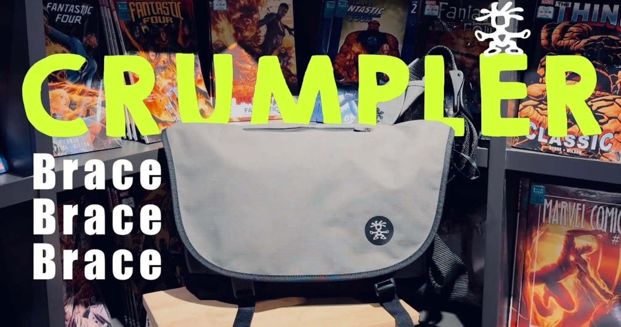 Crumpler Brace Brace Brace messenger bag displayed in front of comic book shelves, featuring a light gray flap, black body, circular Crumpler logo, and bold promotional typography highlighting the model name.