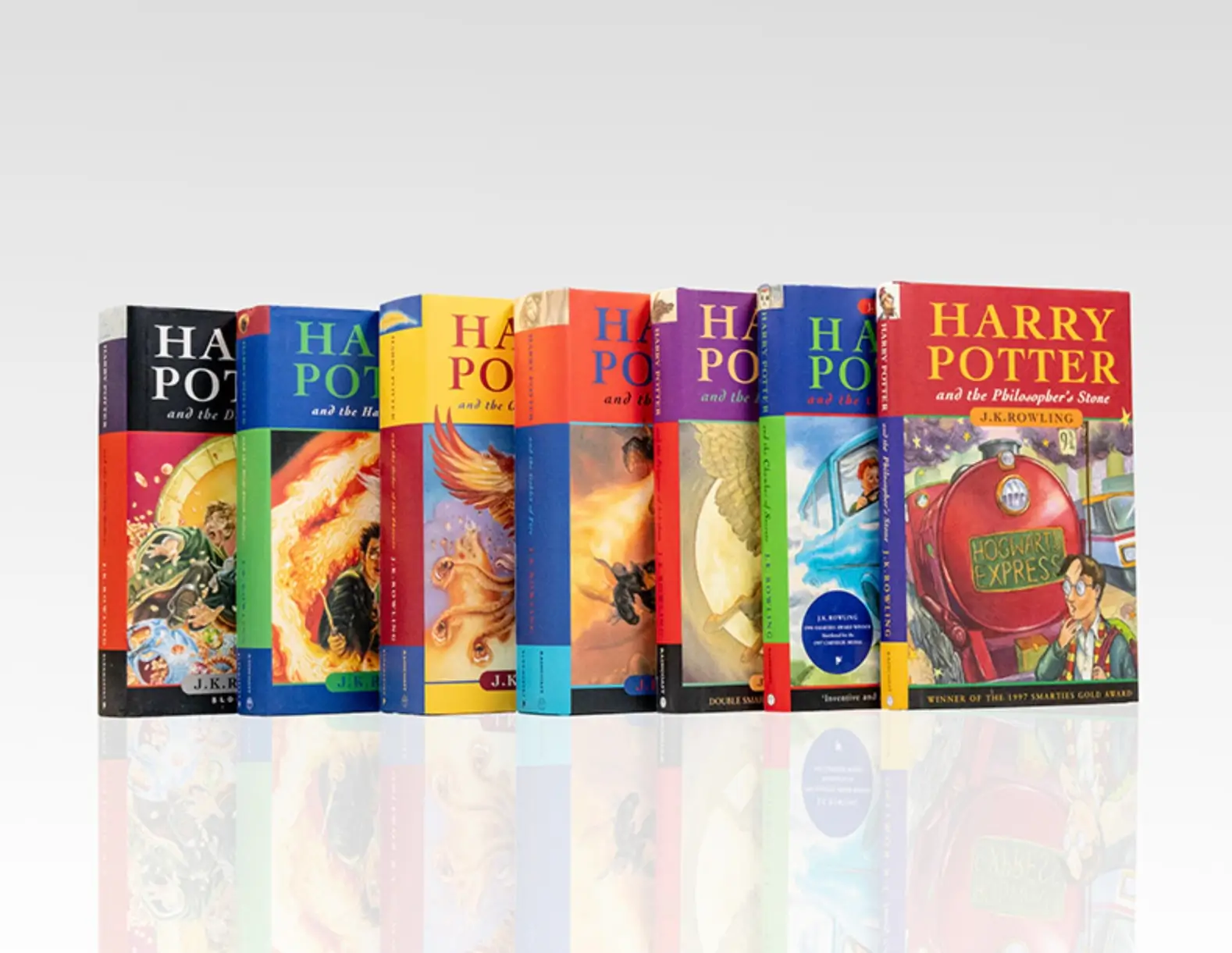 Complete set of seven first edition UK Harry Potter hardcover novels with colorful original dust jackets displayed against a white background.