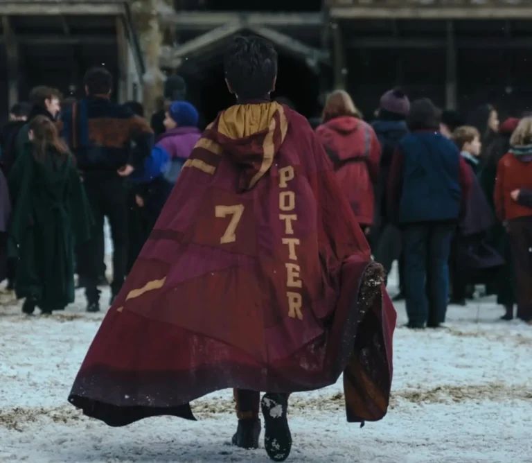 Harry Potter walks across a snowy Hogwarts courtyard wearing a Gryffindor Quidditch cape with "POTTER" and the number 7 on the back