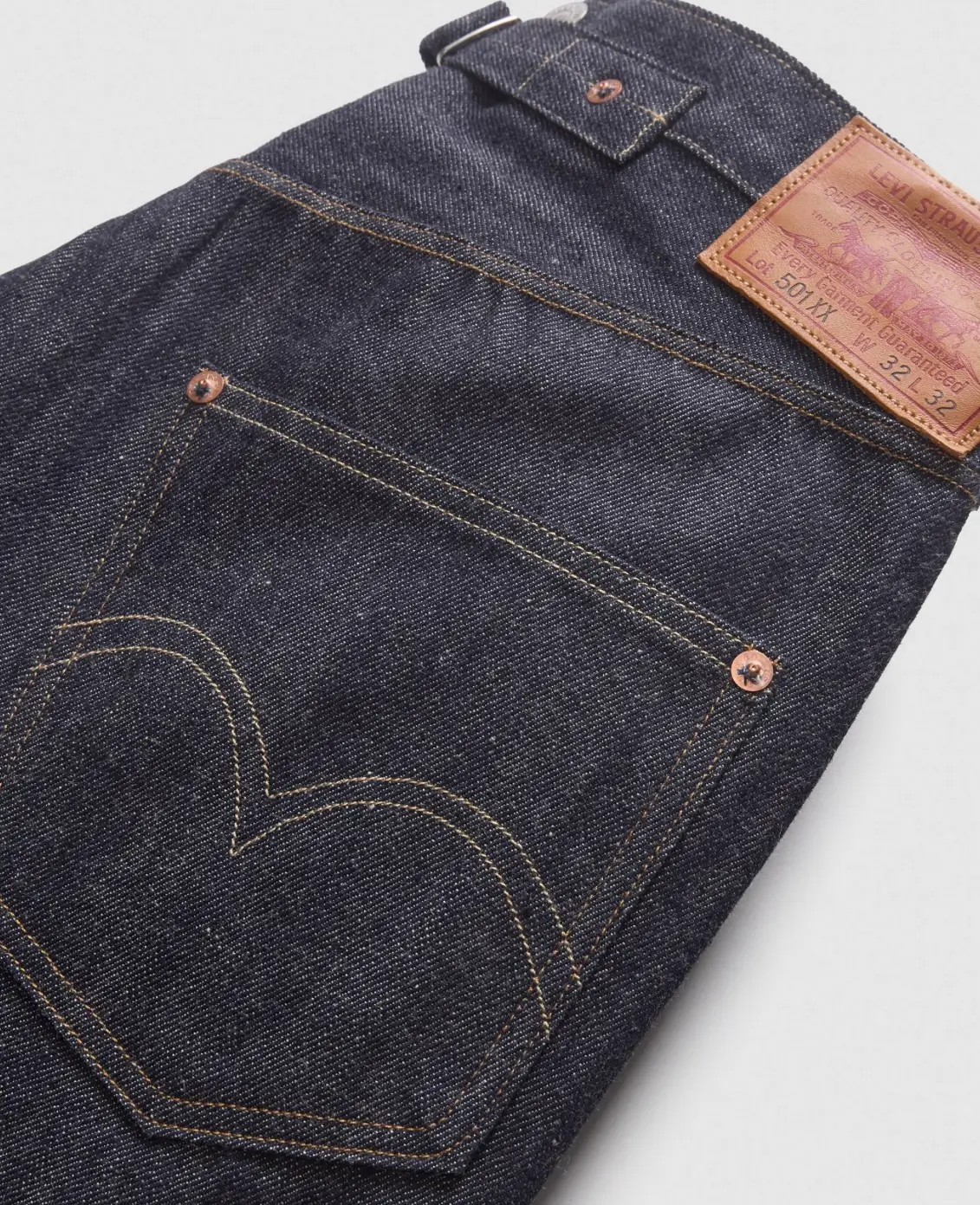 Folded pair of dark indigo Levi's 501 XX selvedge jeans featuring the signature arcuate-stitched back pocket, tan leather Two Horse patch, copper rivets, and heavyweight raw denim with a clean unworn finish.