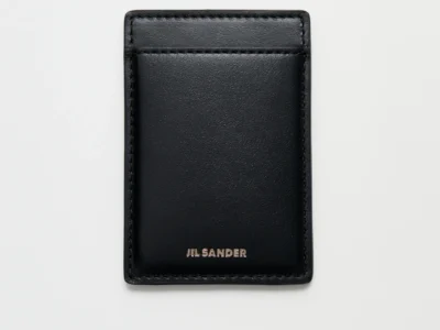 Black Jil Sander leather card holder shown from the reverse side on a clean white background. The minimalist design features a single card slot, smooth leather construction, tonal stitching around the edges, and a silver foil Jil Sander logo centered near the bottom