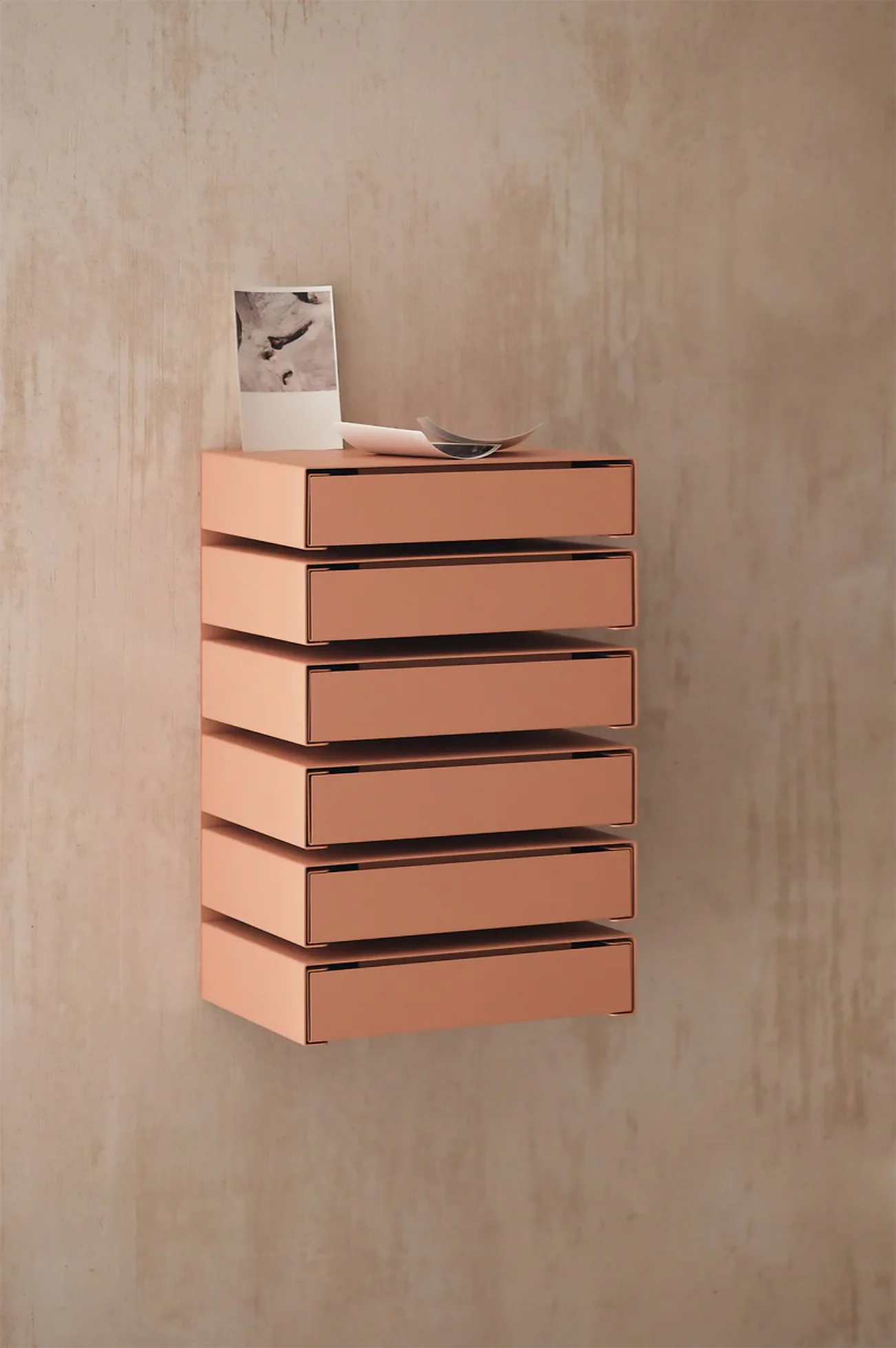 Coral-colored wall-mounted modular aluminum drawer cabinet with six stacked compartments displayed against a textured neutral wall.
